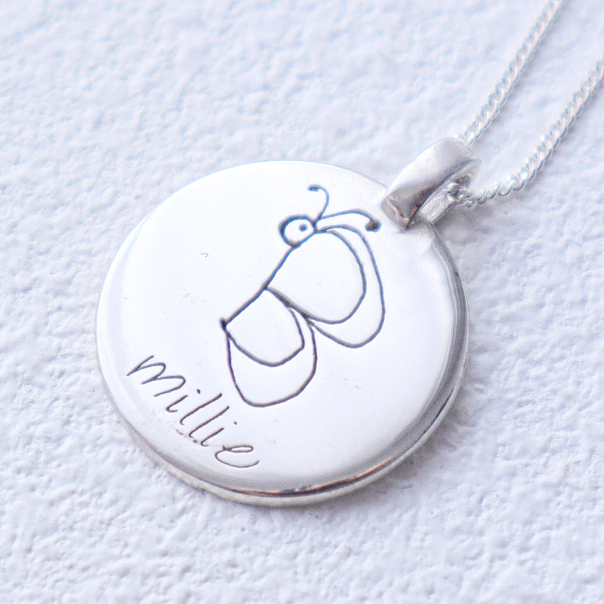silver round pendant with a simple line drawing of a butterfly and the name 